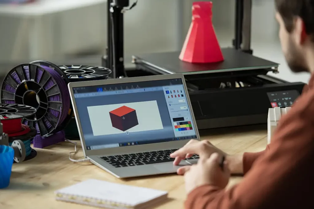 Persona trabajando en su notebook imprimiendo en una impresora 3D